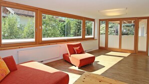 A modern living room with large windows, a red sofa, and a wooden coffee table. - Cosy apartment for 8 guests with WIFI, TV and patio (Taxach)