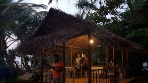 Un espace de restauration extérieur rustique, doté d’un toit de chaume et entouré d’une végétation luxuriante.