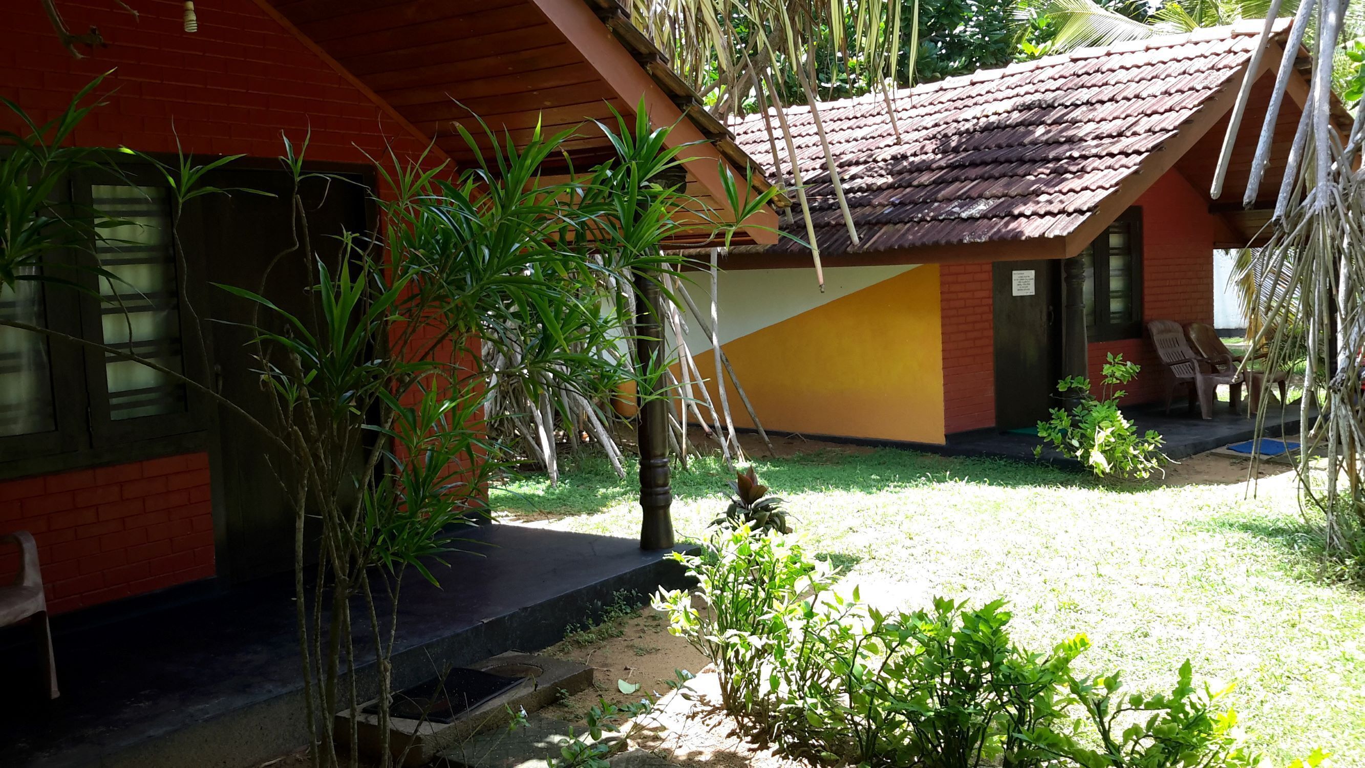 A house with a red and yellow exterior, a tiled roof, and a small garden area with plants and a bench.