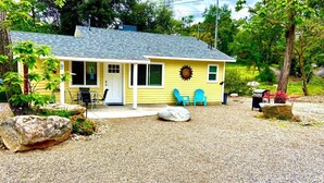 A yellow house with a porch, two blue chairs, and a large rock in the front yard. - Newly remodeled quaint Cottage (Three Rivers)
