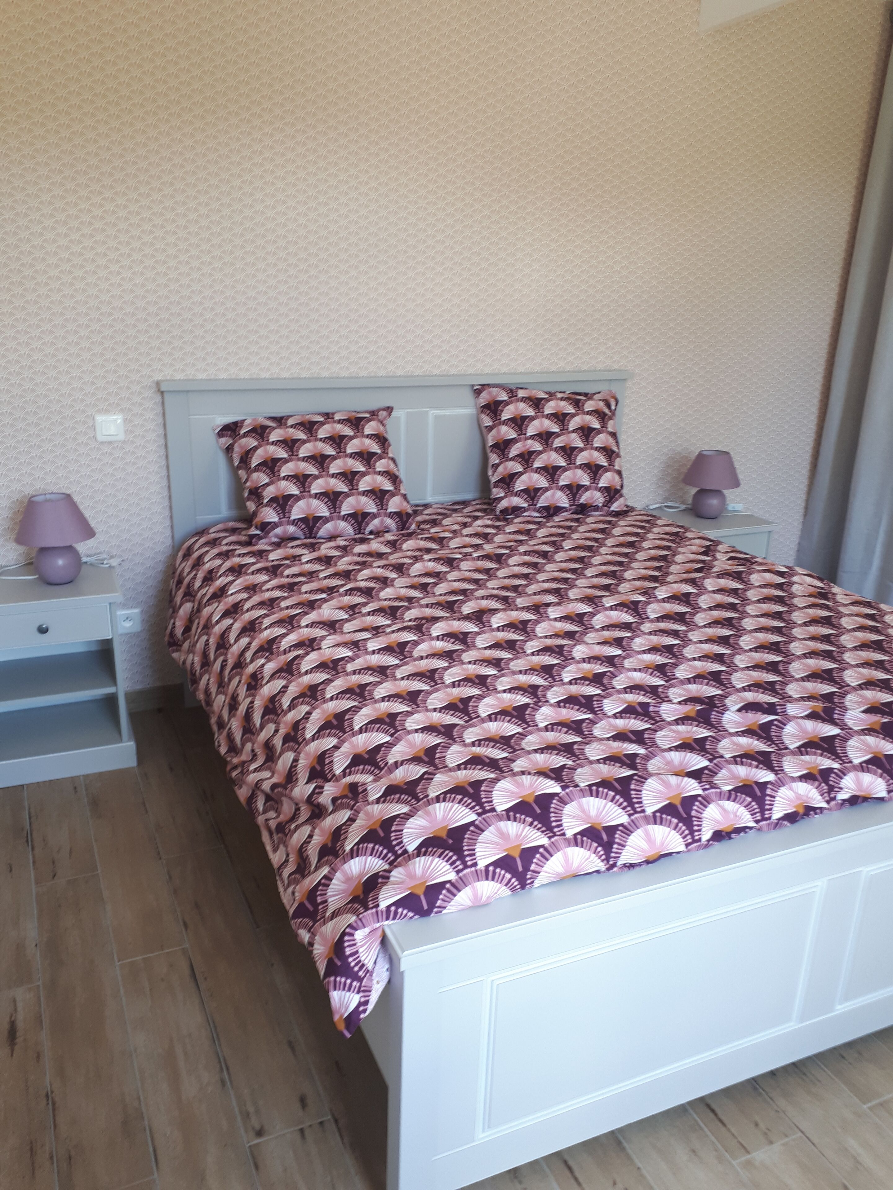 Un lit bien fait, avec une couvre-lit à motifs et des coussins assortis, une table de chevet avec une lampe et une petite table de nuit également dotée d’une lampe.