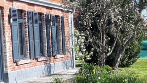 Un edificio de ladrillo con contraventanas, un césped bien cuidado y un árbol con flores blancas.