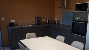 Una cocina compacta con una mesa blanca y cuatro sillas, un horno empotrado y un microondas sobre la encimera.