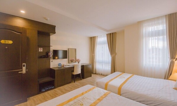 Quarto de hotel com duas camas, uma mesa, televisão e guarda-roupa.