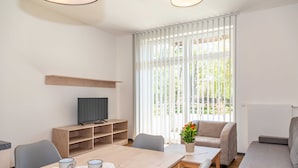 Un salon moderne avec une table à manger en bois, un canapé gris et un téléviseur posé sur un meuble en bois.