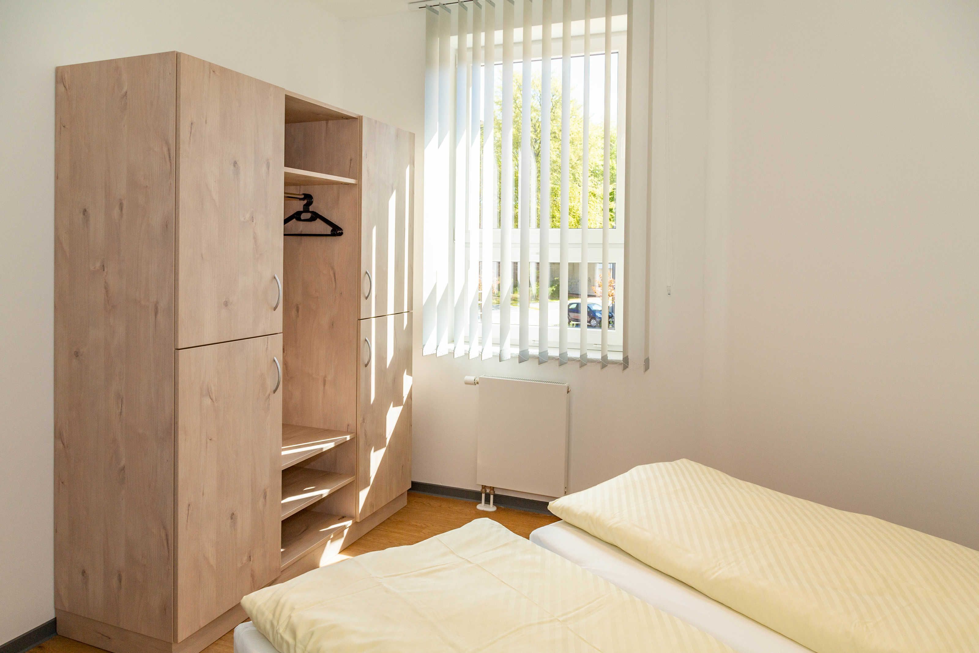 A bedroom with a wooden wardrobe, a radiator, and a window with blinds.