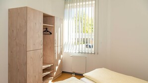 Une chambre avec une armoire en bois, un radiateur et une fenêtre avec des stores.
