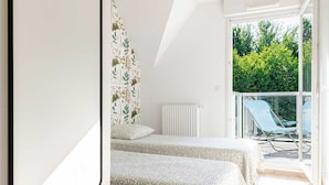 Ein Schlafzimmer mit zwei Betten, einem Balkon und Blick auf Grünflächen sowie einer weißen Decke.