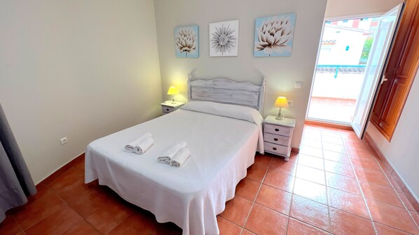 Un dormitorio con una cama, dos mesitas de noche con lámparas, y tres cuadros de flores colgados en la pared.