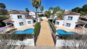 Um resort com edifícios de dois andares, um caminho central e duas piscinas.