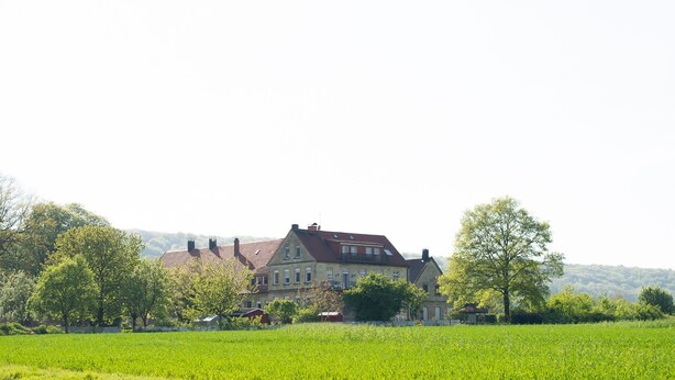 A large, two-story house with a red roof, surrounded by a green field and trees. - Apartment No. 2 in the Main House – bright, cozy, and well equipped (Havixbeck)