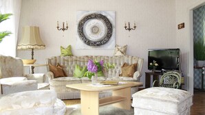 A living room with a sofa, armchairs, a coffee table, a TV, and a decorative plate on the wall.