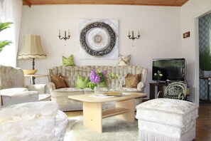 A living room with a sofa, armchairs, a coffee table, a TV, and a decorative plate on the wall.