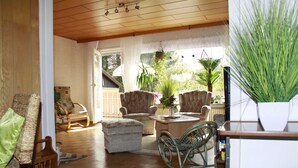 Un salon chaleureux, doté de meubles en osier, d’un plafond en bois et offrant une vue sur l’extérieur.