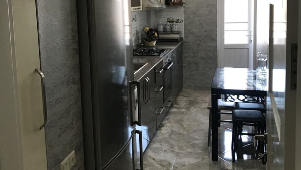 A modern kitchen with stainless steel appliances, a central island, pendant lighting, and a view to the dining area. - 4 rooms apartment  (Batumi)