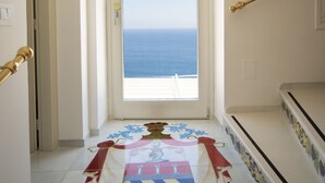 A hallway with a view of the sea, a chandelier, and a floor with a family crest.