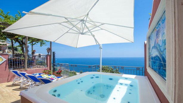 A hot tub with a view of the sea, a white umbrella, and blue lounge chairs.