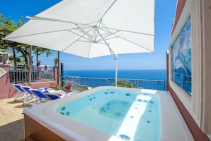 Ein Whirlpool mit Meerblick, ein weißer Sonnenschirm und blaue Liegestühle.