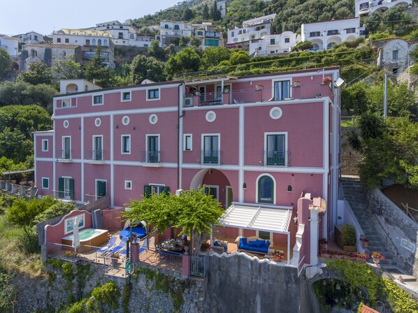 A multi-story pink building with balconies, a rooftop terrace with seating, and a stone retaining wall. - Palazzo Rocco - Villa Sunshining NEW - 4 rooms/4 bath -10 Pax - Heated Jacuzzi (Praiano)