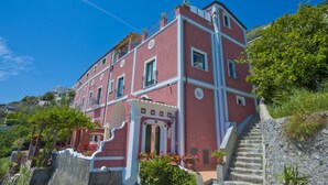 A multi-story building with a pink facade, a staircase leading to the entrance, and a garden area with potted plants.