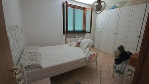 A bedroom with a single bed, a chair, a wardrobe, and a window with blinds.