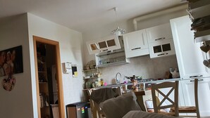 A kitchen with white cabinets, a stove, and a dining area with a chair and table.