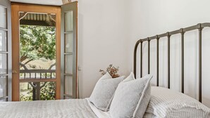 A bedroom with a bed, white bedding, a wooden door with glass panels, and a view of greenery outside. - Be amongst nature in the 1890s farmhouse - a time you will never forget. (Tugrabakh)