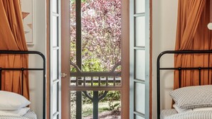 A room with two beds, a wooden door with a metal gate, and a view of a garden with trees. - Be amongst nature in the 1890s farmhouse - a time you will never forget. (Tugrabakh)