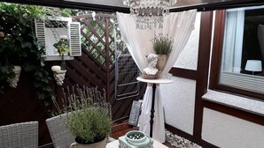 Un patio con sillas de mimbre, una mesa con adornos, una lámpara colgante y vistas a un jardín.