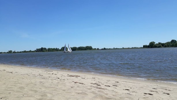 Una playa arenosa con un velero a lo lejos.
