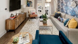 Un salon comprenant un canapé, une table basse, un téléviseur fixé au mur, un meuble en bois et un mur décoré d’un motif.