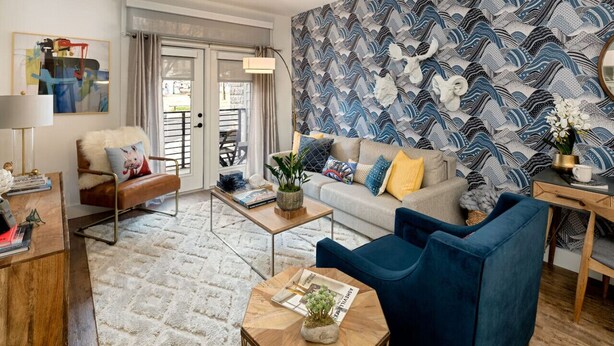 Un salon moderne avec un canapé, des fauteuils, une table basse et un mur décoré d’un motif.