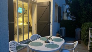 En udendørs terrasse med et rundt bord og stole, en skydedør til et indre rum og en potteplante på bordet.