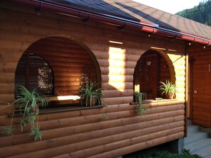 Cozy cabin with arched windows and a rustic charm, featuring a red roof and potted plants.