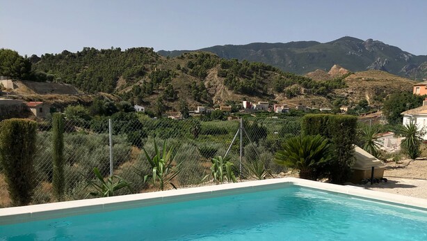 Une piscine d’un bleu éclatant, avec vue sur un paysage vallonné et des maisons en arrière-plan.