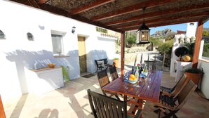 Une terrasse extérieure avec une table et des chaises en bois, un pot de fleurs et une vue sur une montagne.