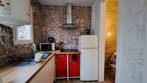 A compact kitchen with a microwave, stove, and refrigerator. A window provides natural light, and the walls are decorated with patterned tiles. - Casa Mia Barcelona & Barça (Hospitalet de Llobregat)