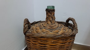 A large woven basket with a handle and a green lid, placed on a wooden floor against a white wall. - Casa Mia Barcelona & Barça (Hospitalet de Llobregat)