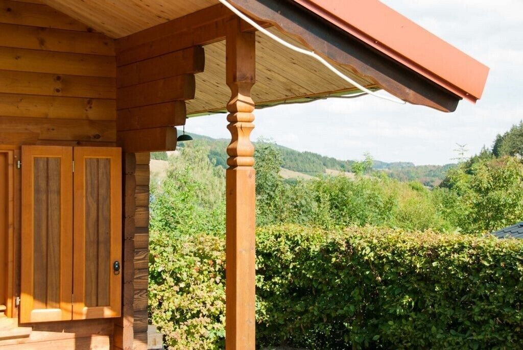 A wooden cabin with a porch, a door, and a view of a green landscape.
