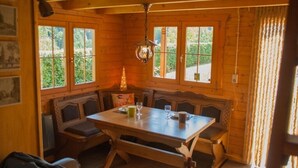 Een gezellig houten interieur met een eettafel, bankjes en grote ramen.