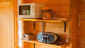 Een houten interieur met een magnetron op het bovenste plankje, een radio op het middelste plankje, en een afstandsbediening op het onderste plankje.