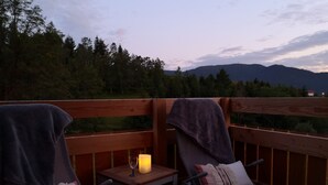 Eine Terrasse mit zwei Liegestühlen, einem kleinen Tisch und einer Kerze. Die Terrasse bietet Blick auf eine bewaldete Gegend mit Bergen im Hintergrund.