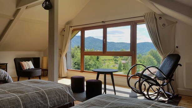 Ein Schlafzimmer mit großem Fenster, einem Bett, einem Sessel und einem kleinen Tisch.