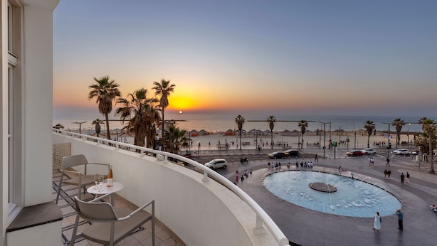 Un balcón con mesa y sillas con vista a una playa al atardecer.