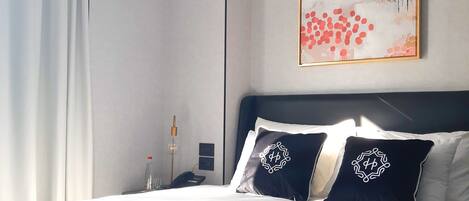 A modern hotel room with a large bed, a nightstand, a phone, and a painting on the wall.