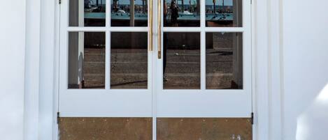 A double door entrance with a black mat reading "The Herbert Tel Aviv" and a clear view of the beach and street through the glass.