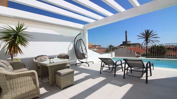 Eine Dachterrasse mit Korbmöbeln, einem Pool und Blick auf einen historischen Turm.