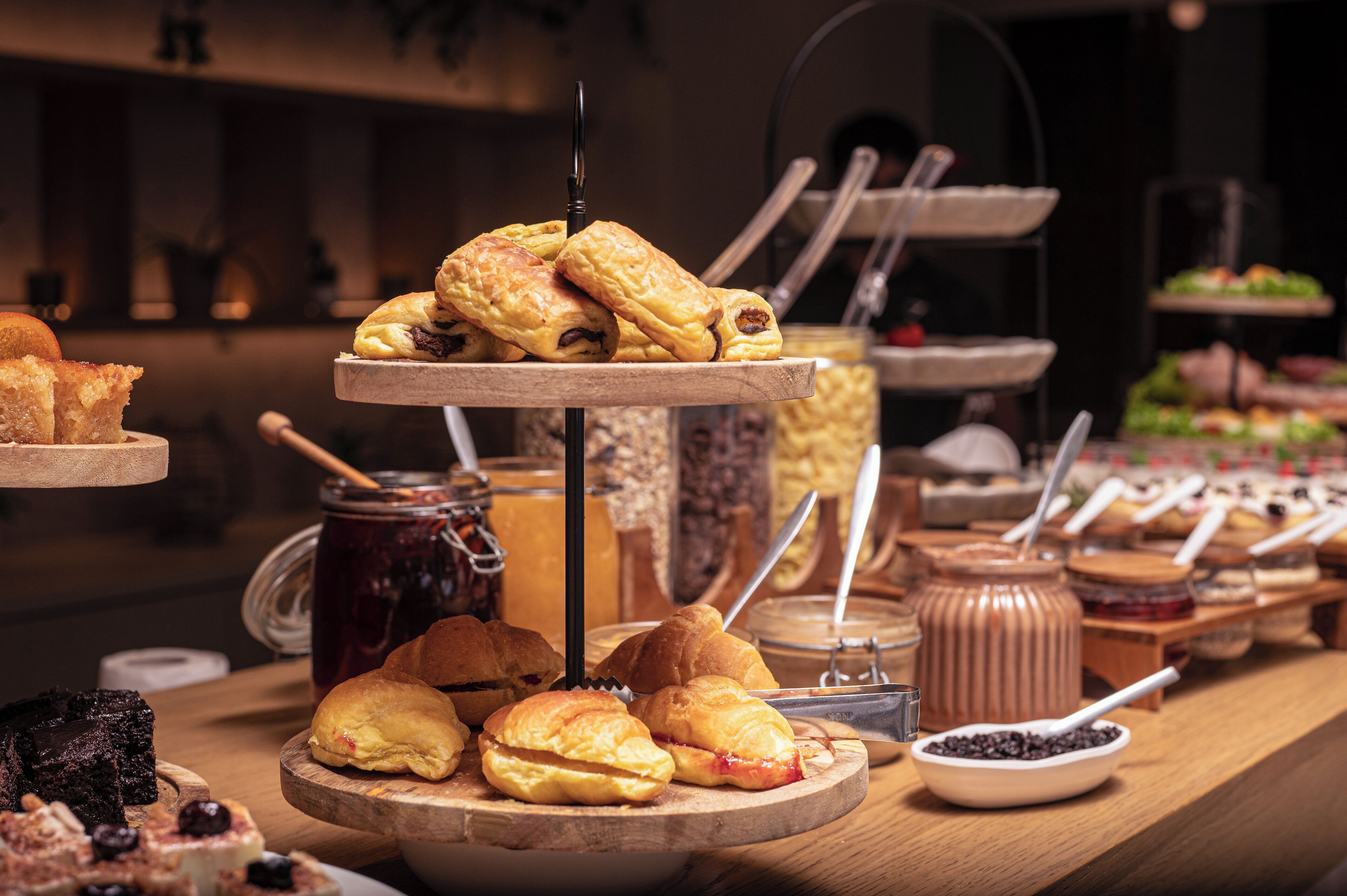 A buffet with various pastries and desserts, including croissants and bread, arranged on wooden boards.
