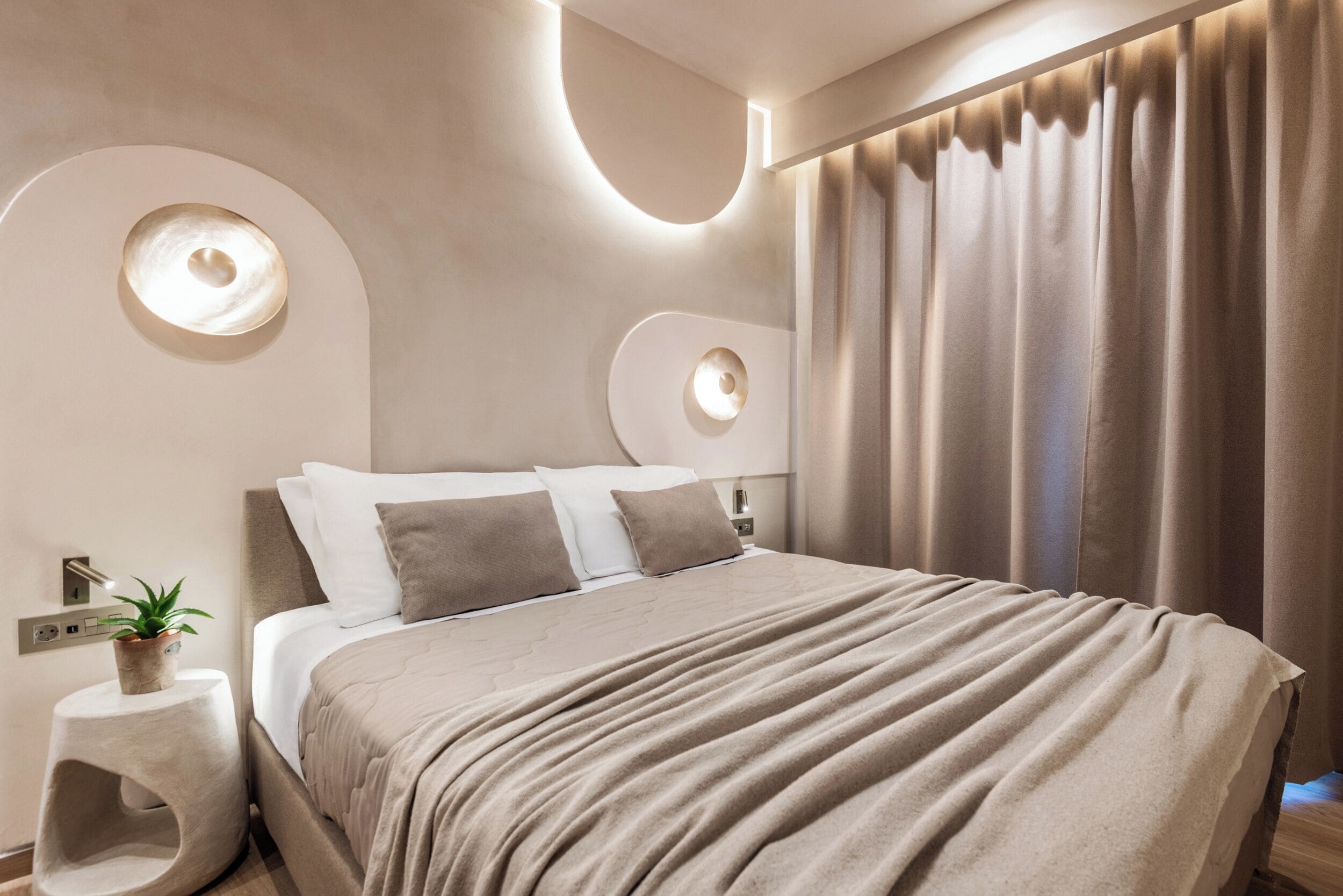 Ein modernes Schlafzimmer mit einem großen Bett, einem Nachttisch mit Pflanze und einer Wandleuchte.