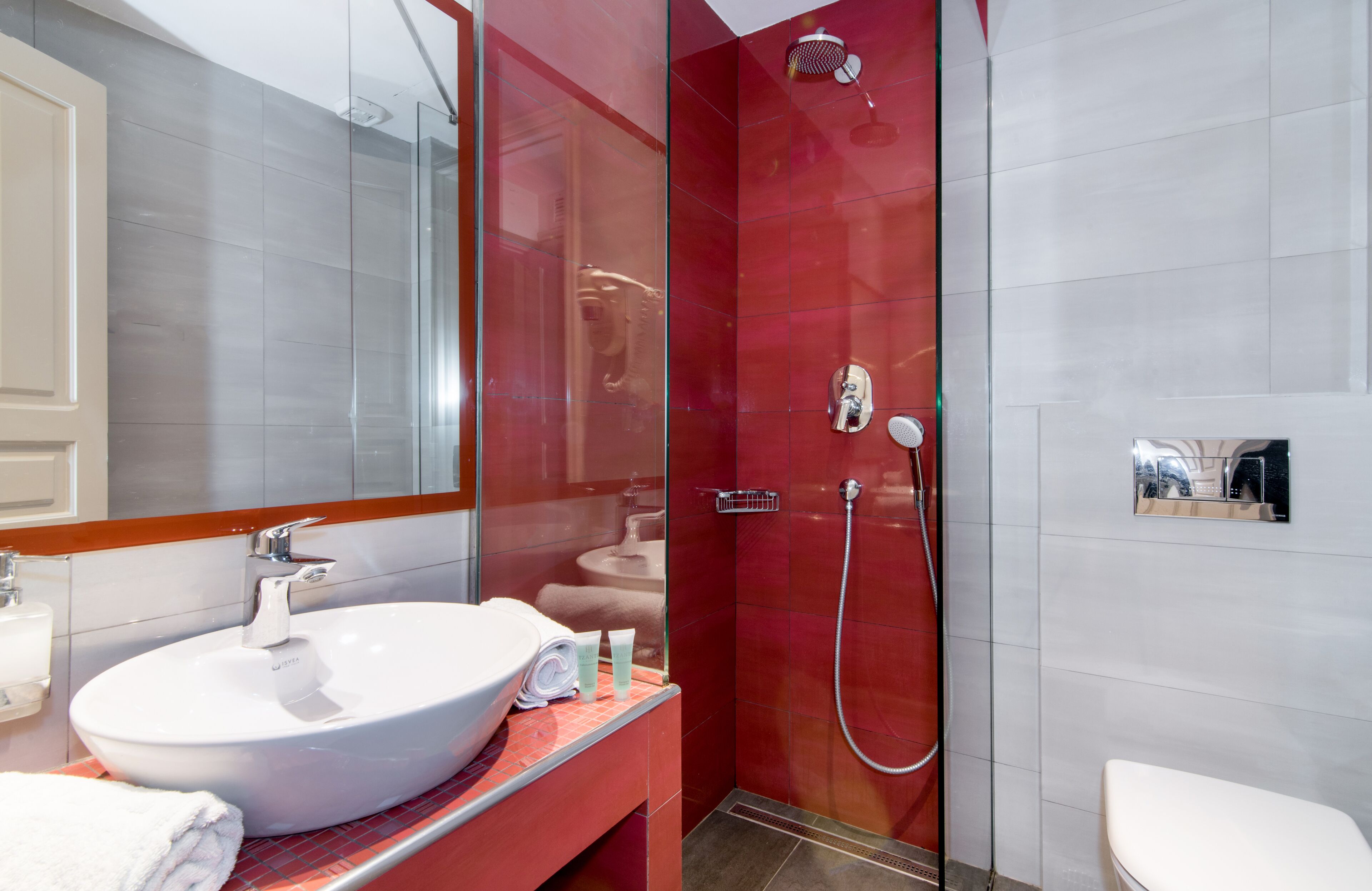 Un baño moderno con un lavamanos grande de color blanco, cabina de ducha con mampara de vidrio y pared con azulejos rojos.